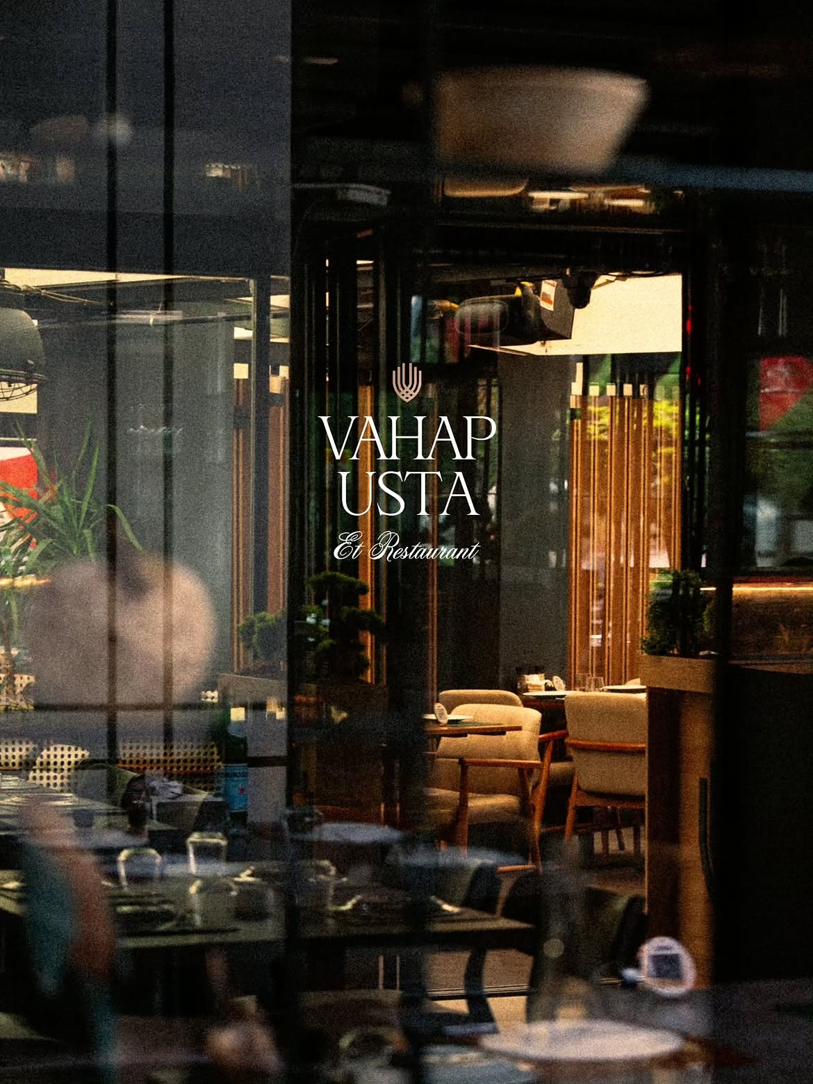 Vahap Usta Et Restaurant logolu cam ardından kurulu masalar, bej sandalyeler ve ahşap detaylı loş iç mekân