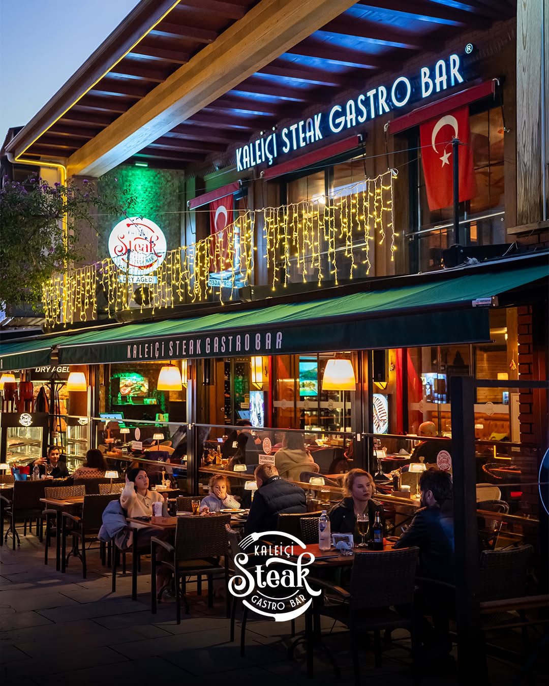 Kaleiçi Steak Gastro Bar'ın akşam ışıklı cephesi, Türk bayrakları ve dış masalarda oturan misafirler