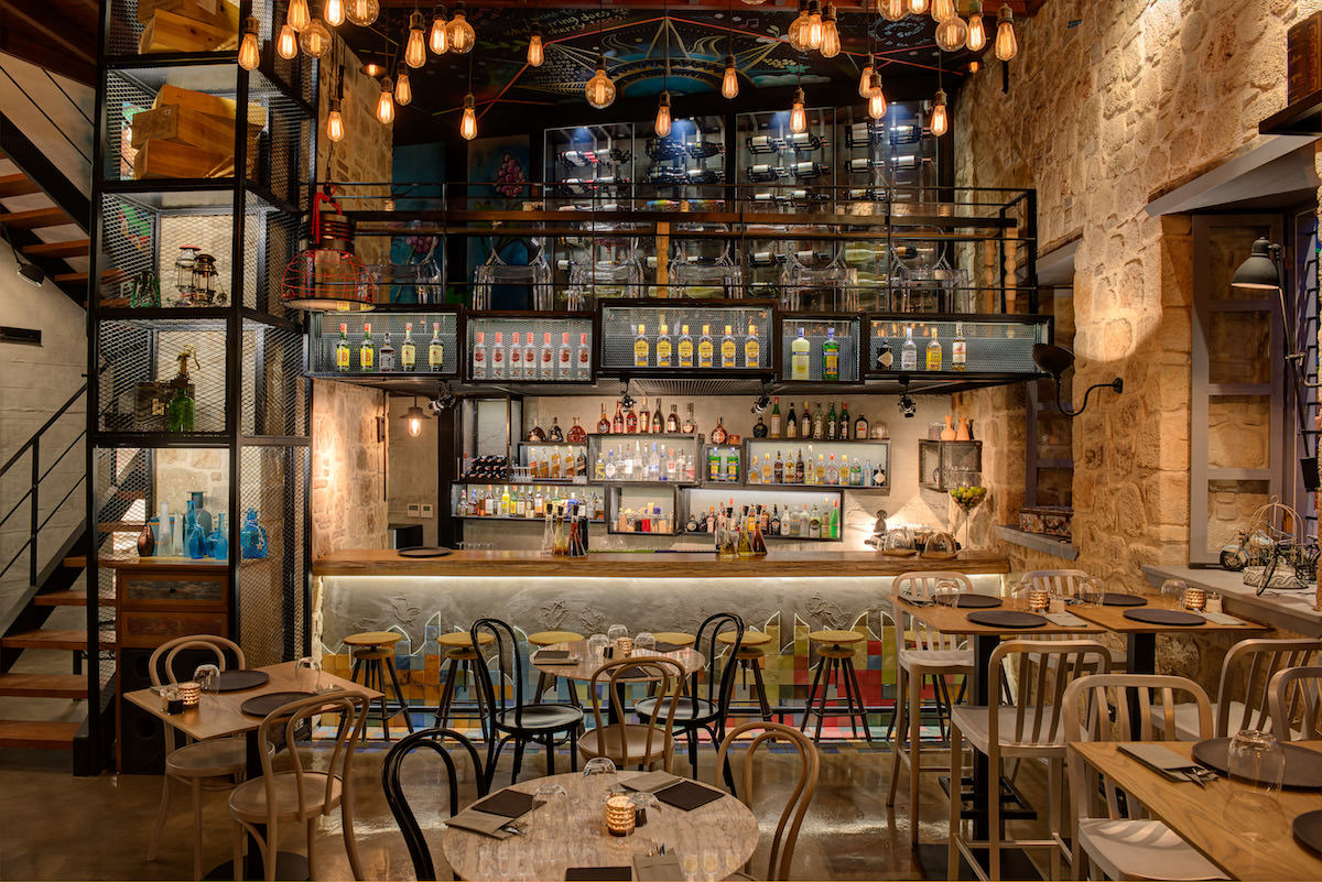 Pio Gastro Bar & Bistro'da taş duvarlı salon, içki şişeleriyle dolu bar, sarkıt ampuller ve kurulu masalar
