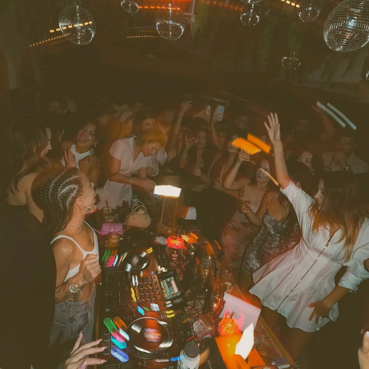 Off Cocktail Bar'da disko topları altında DJ masası başında bir DJ ve etrafında dans eden kalabalık