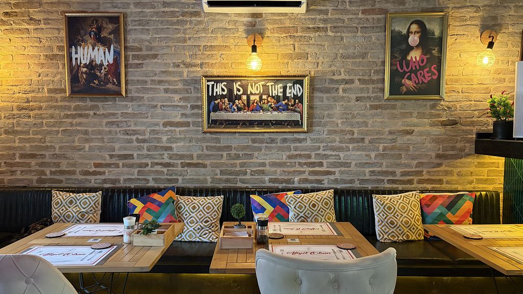 LEVEL restoranında tuğla duvarda pop-art tablolar, renkli yastıklı koyu yeşil koltuk ve ahşap masalar
